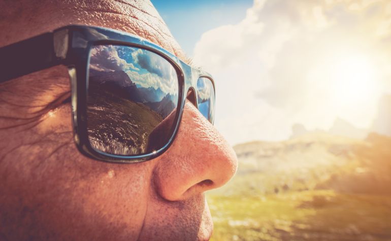 Symptoms of Sunglasses Protectation. Caucasian men in his 50s in the Trendy Black Sunglasses. Closeup Photo. Mountains Reflection in the Lenses.