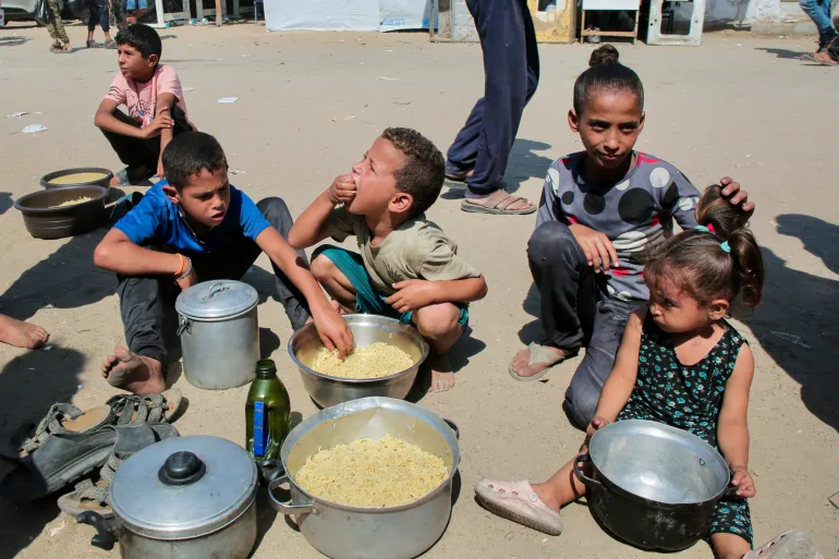 TOPSHOT - Palestinian children eat cooked rice after managing to get portions of hot food from a charity kitchen in Khan Yunis in the southern Gaza Strip on August 27, 2025.