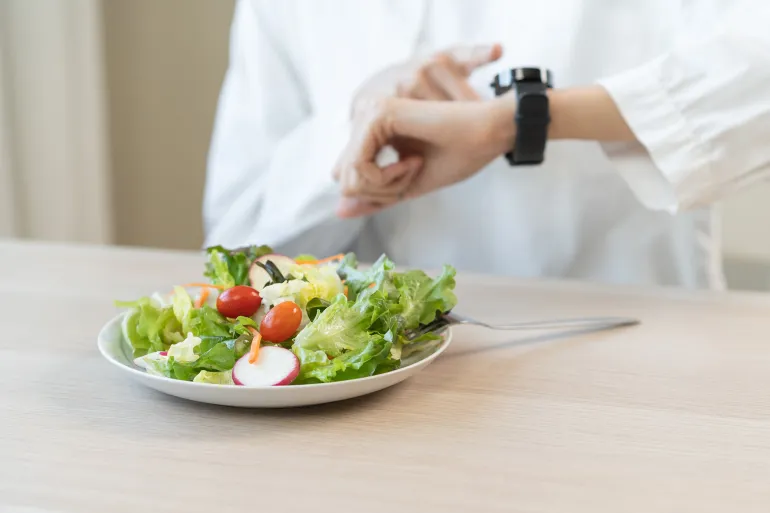Intermittent fasting, healthy asian diet young woman dietary watching wrist watch, temptation hungry of brunch food in morning on table at home, waiting time to eat salad but not yet first meal time.; Shutterstock ID 2672382717; purchase_order: aj; job: ; client: ; other: