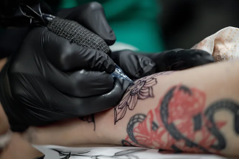 The tattoo artist creates a picture on the body of a man. close-up of tattoo machines and paints