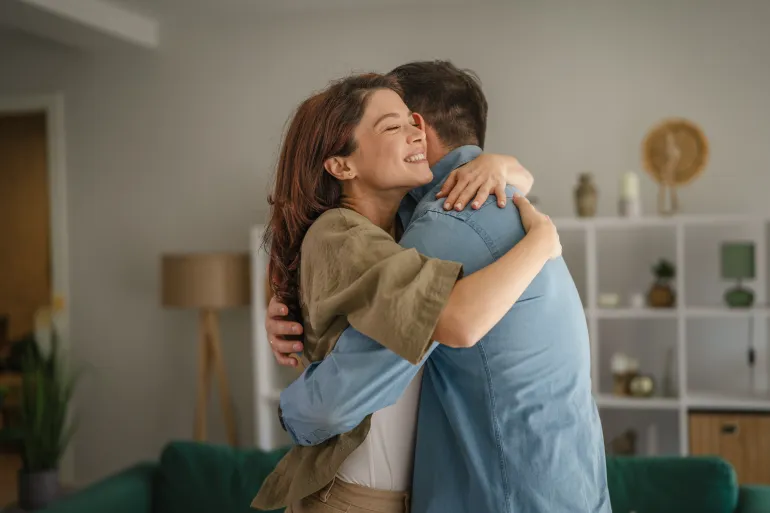 Happy couple embracing in a warm, loving hug at home, sharing a moment of affection, connection, and togetherness in their living room, representing comfort and reunion