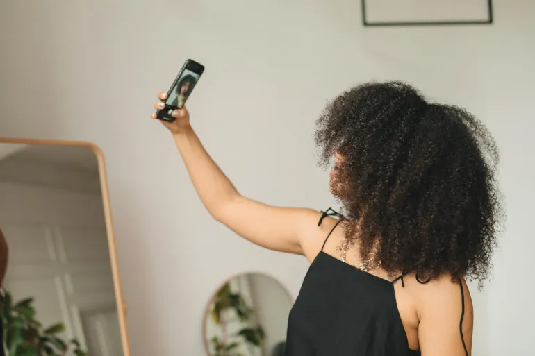 A woman with curly hair takes a selfie in front of a mirror at home, capturing a candid moment.