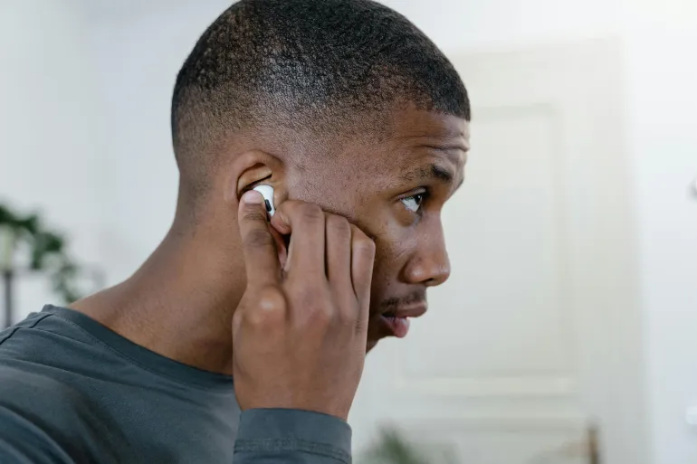 Close-up of a man adjusting his wireless earbuds while indoors, showingcasing modern lifestyle.