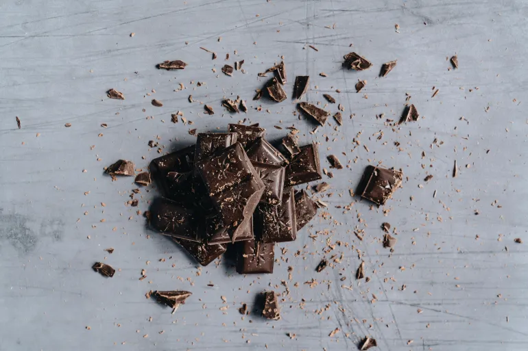 Top-down view of broken dark chocolate bars with shavings on a gray background, ideal for food photography.