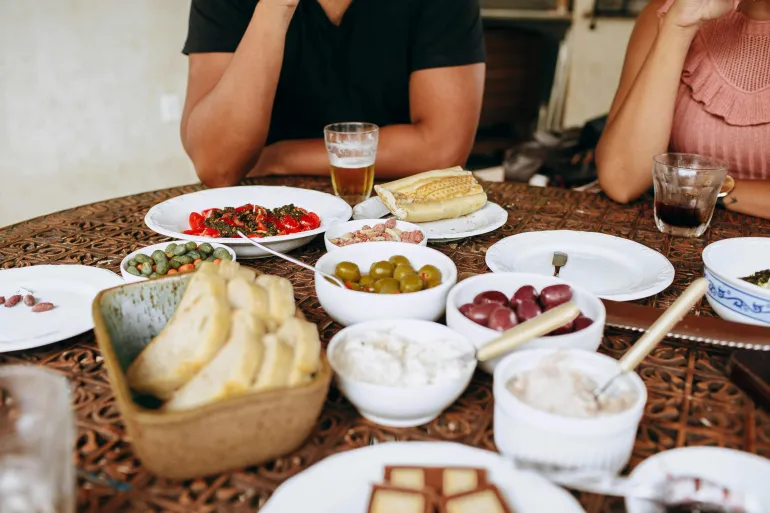 A variety of Mediterranean dishes on a table with bread, olives, and drinks for a casual gathering.