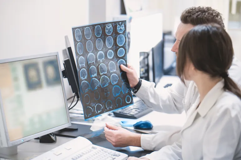 Two doctors, a man and a woman doctor, examine an MRI image of the brain in an MRI room. Blurred image