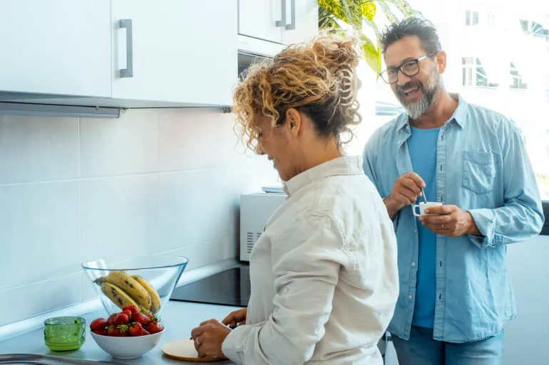 Man and woman in relationship living together talking happily in the kitchen. Adult man and woman preparing breakfast. Morning routine family inside home. One couple enjoying apartment and smiling