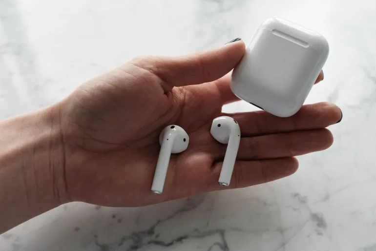 A woman's hand holding wireless earbuds and a charging case on a marble surface.