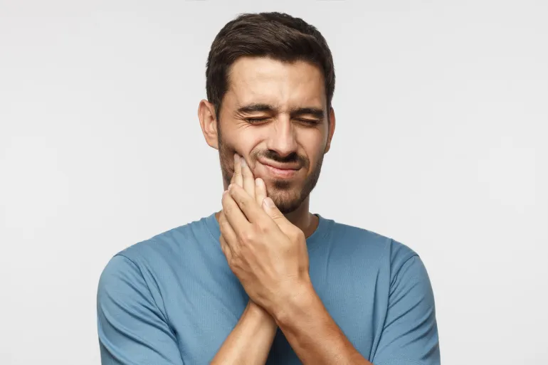 Toothache. Young man feeling pain, holding his cheek with both hands, suffering from bad toothache, having painful expression