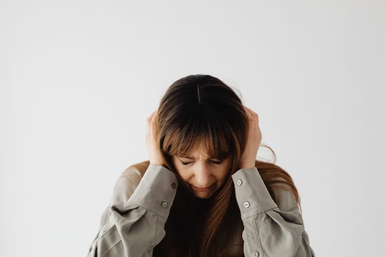 Woman with closed eyes holding her head, conveying stress and emotions against a plain white background.