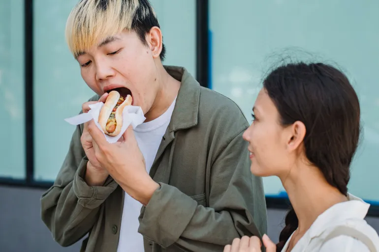 Asian couple sharing a moment while enjoying a delicious street food snack outdoors.