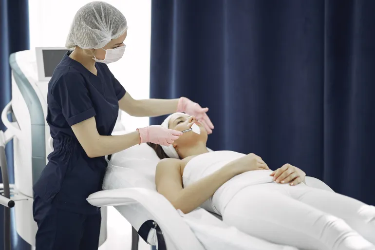 Aesthetician applies facial treatment to a relaxed woman in a modern spa clinic setting.