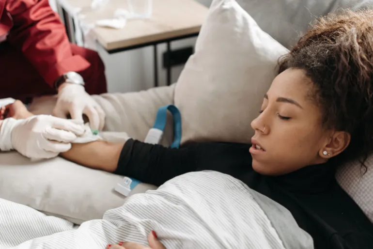 Paramedic providing medical care to an ill woman resting on a couch indoors.