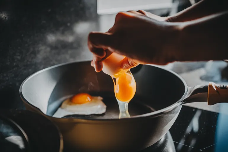 Close-up of female hand cracking an egg into a sizzling hot frying pan as she prepares a healthy breakfast in the kitchen in the morning. Clean eating and healthy eating habits with natural ingredients. Wellness lifestyle and mindful meal preparation
