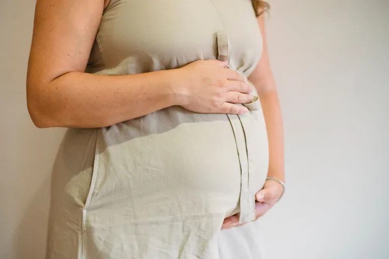 Close-up of a pregnant woman gently cradling her belly, showing maternal affection and anticipation.