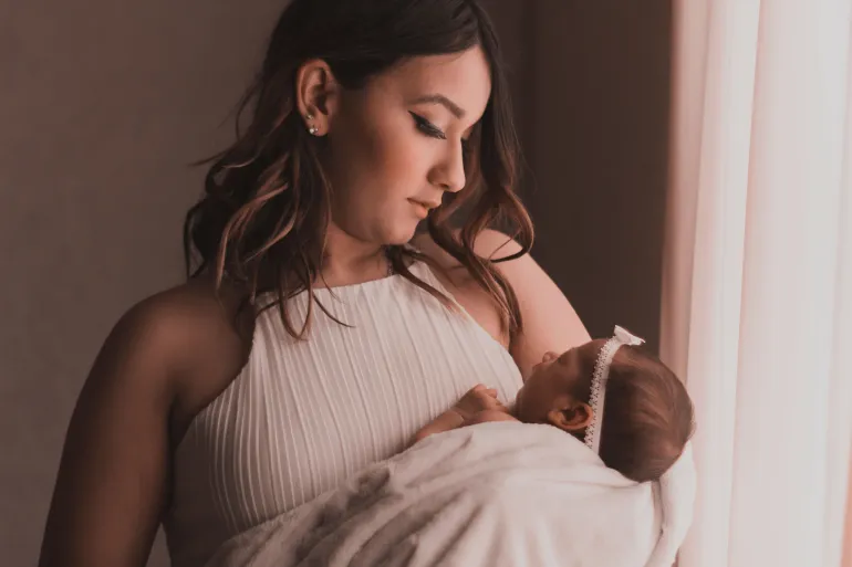 A mother lovingly cradles her baby by a window, capturing a tender moment.