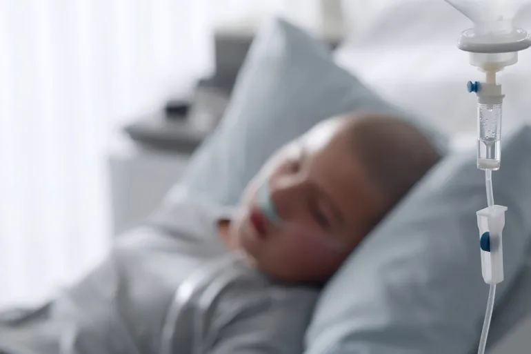 Focus on intravenous drip with sick kid lying in hospital bed on background. Teen boy patient with cancer resting in bed having medication in dropper; Shutterstock ID 1921349711; purchase_order: aj; job: ; client: ; other: