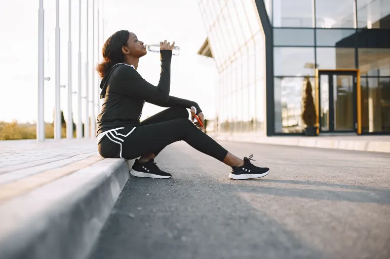 An African American woman takes a break during her workout to hydrate with a water bottle.