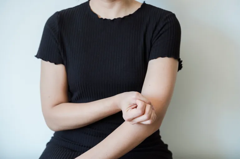 A close-up view of a woman in a black shirt holding her arm, showing skin contact and emotion.